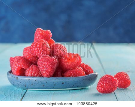 Fresh raspberries on blue wooden background. Raspberry in blue trandy plate. Summer and healthy food concept. Copy space.