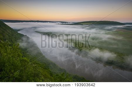 Top view of Dnestr (Dniester) river at sunrise. River is covered with mist and surrounded with green forest and fields.
