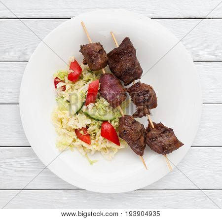 Pork shashlik and vegetable salad on a garnish. Healthy food, picnic, lunch dish concept. White wooden planks background.