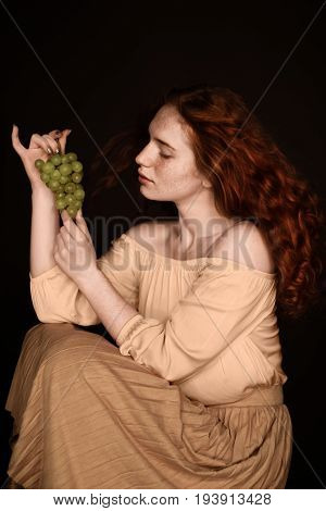 attractive sensual redhead woman posing with green grapes isolated on black