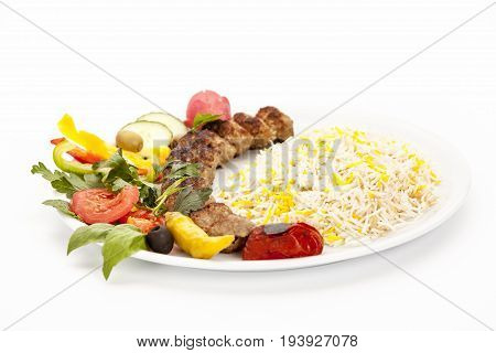 Low angle view of a grilled lamb kebab kubide served with rice pepper tomato and herb on a simple plate. Well roasted ground meat balls taken off the skewer. Studio shot over white background.