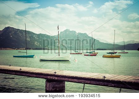 Small sailboats anchoring in alpine lake. Landing stage and mountains framing the boats. Bavaria, Germany, Allgau, Forggensee. Retro vintage style.