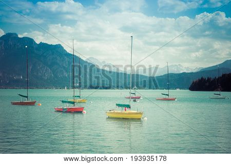 Small colorful sailboats anchoring in turquois alpine lake in front of mountains. Bavaria, Germany, Allgau, Forggensee. Retro vintage style.