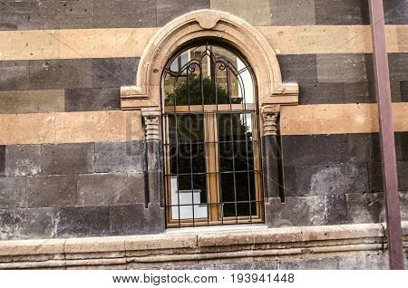 Arched window openings with carved columns and decorative steel grille on the facade stone wall of old building