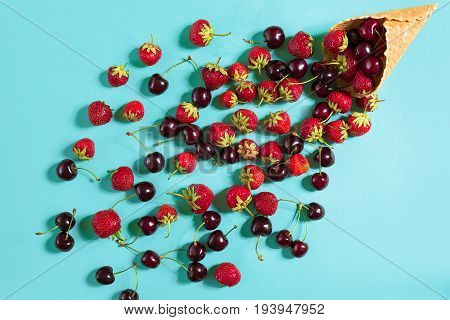 Berries in waffle cone - strawberry and black cherry on blue background. Top view. Copy space. Still life mockup flat lay
