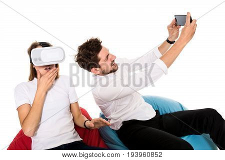 Smiling friends experiencing virtual reality glasses seated on beanbags isolated on white background. Experiencing virtual gaming adventure. VR