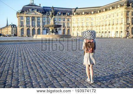 Young woman tourist standing back enjoying view on the famous Bourse square with beautiful buildings and fountain in Bordeaux city during the morning