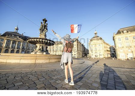 Young woman tourist enjoying morning view on the famous Bourse square standing back with french flag in Bordeaux city in France