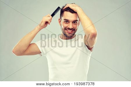 beauty, grooming and people concept - smiling young man brushing hair with comb over gray background