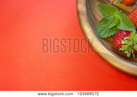 Tasty strawberries and a mint leaf in a wooden plate on a red background. Top view cpmposition. Place for text.