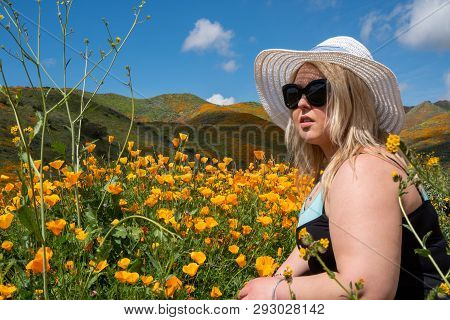 Blonde Woman Wearing A Straw Bonnet Hat Looks Out To The Field Of Poppy Wildflowers During The Super