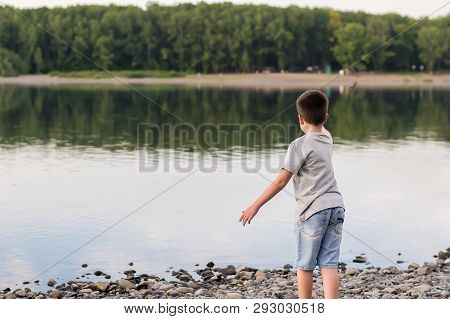 A Child, A Teenager, On A Stony Shore Throws Stones Into The River, Lake