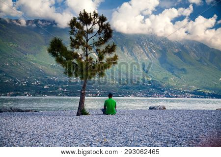 Young man sitting in front of mountain and lake landscape at Garda Lake, Italy. - Travel, summer vacacion concept.