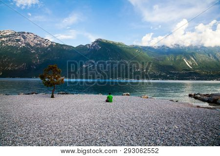 Young man sitting in front of mountain and lake landscape at Garda Lake, Italy. - Travel, summer vacacion concept.