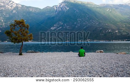 Young man sitting in front of mountain and lake landscape at Garda Lake, Italy. - Travel, summer vacacion concept.