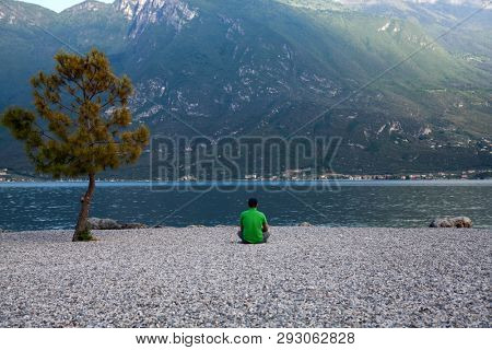 Young man sitting in front of mountain and lake landscape at Garda Lake, Italy. - Travel, summer vacacion concept.