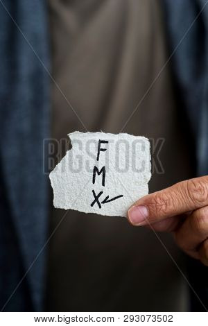 closeup of a young caucasian person holding a piece of paper with the letters F for female, M for male and X for the third gender category, written in it, with a check mark on the X