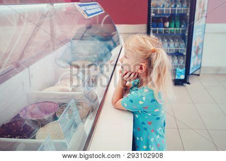 Caucasian Funny Blonde Child Girl Looking At Ice Cream In Shop Window Trying To Choose One. Kid With