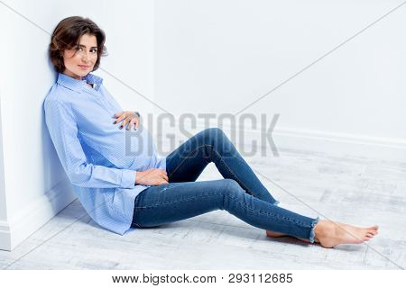 A beautiful pregnat woman sitting in a studio. Motherhood. Fashion for pregnant women