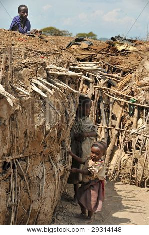 OLDUVAI GORGE, TANZANIE, PROSINEC 23, 2011, MLADÝ MASAJOVÉ MUŽ A DĚTI STOJÍCÍ POBLÍŽ JEJICH CHATY