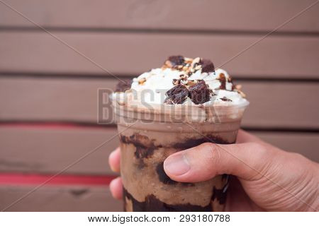 A Delicious Chocolate Frappe In Plastic Cup In Hand