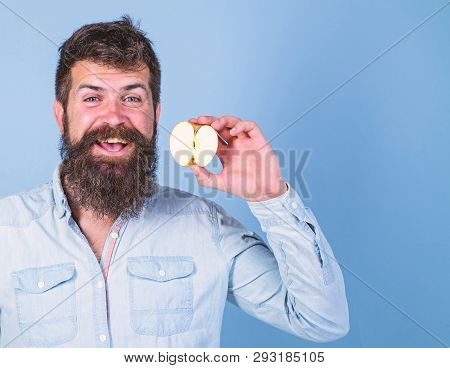 Man Bearded Smiling Holds Apple Blue Background. Half Of Apple Healthy Lifestyle. Hipster Demonstrat