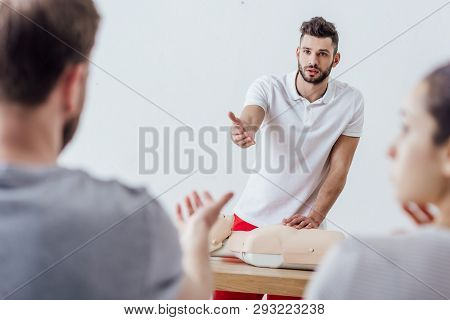 Handsome Instructor With Cpr Dummy Gesturing During First Aid Training Class