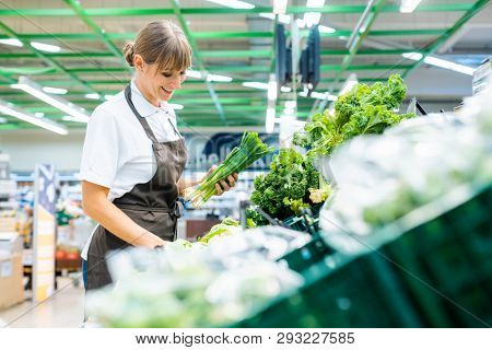 Shop assistant in supermarket re-stocking fresh vegetables into boxes