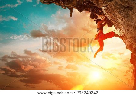 Athletic Woman Climbing On Overhanging Cliff Rock With Sunset Sky Background