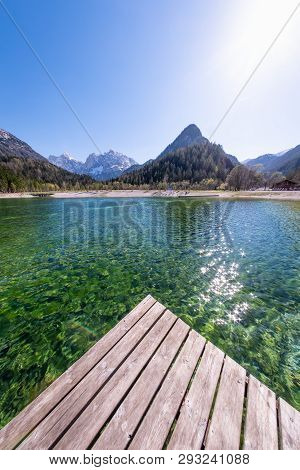 Wooden Dock On Lake Jasna With Mountains Razor And Prisojnik On The Horizont In Slovenia
