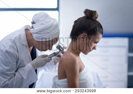 Side view of a mature mixed race female doctor checking the body of a Caucasian female patient with dermatoscopy in a clinic