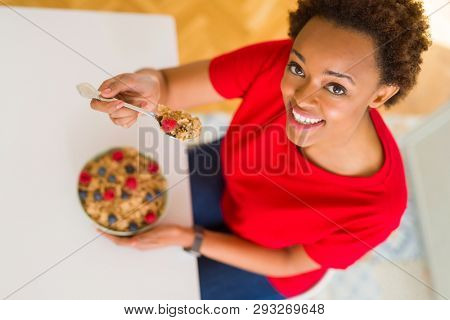 Young beautiful african american woman with afro hair eating healthy wholemeal cereals and berries as healthy breakfast