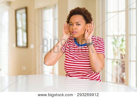 Young beautiful african american woman at home Trying to hear both hands on ear gesture, curious for gossip. Hearing problem, deaf