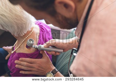 High angle view of Caucasian male dermatologist examining senior patient through dermatoscopy