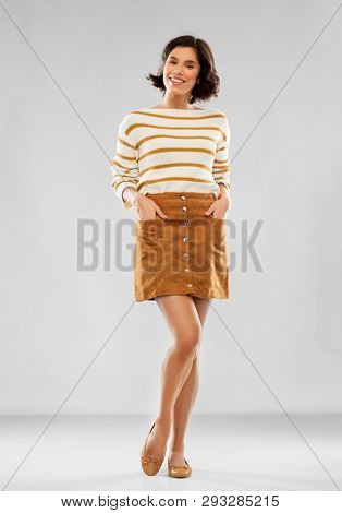 people concept - happy smiling young woman in striped pullover, short skirt and ballet flat shoes posing over grey background