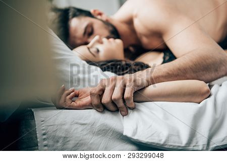 Selective Focus Of Passionate Man Holding Hands With Woman While Lying On Bed