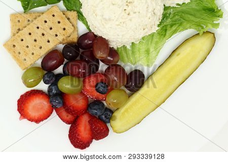 Fresh ripe fruit served with pickle spears, chicken salad and crackers over white.