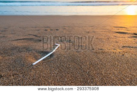 A single plastic straw on a beach at sunset, plastic pollution concept