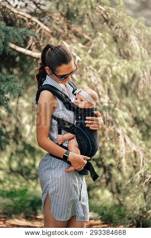 Little Baby Girl And Her Mother Walking Outside Babywearing In The Ergo Carrier Concept