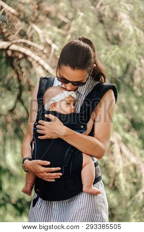 Little Baby Girl And Her Mother Walking Outside Babywearing In The Ergo Carrier Concept