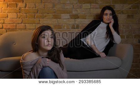 Closeup Portrait Of Two Young Pretty Girls Watching Tv With Curious Facial Expression While Resting 