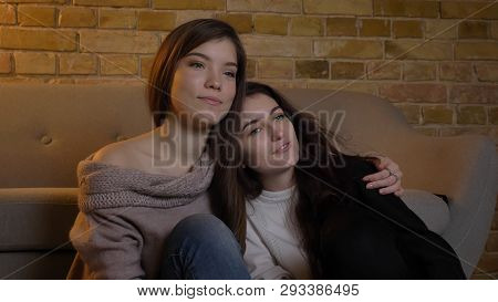 Closeup Portrait Of Two Young Pretty Women Hugging And Watching Tv In A Cozy Apartment Indoors