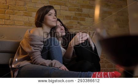 Closeup Portrait Of Two Young Pretty Women Hugging And Watching Tv Chilling With Wine Sitting On The