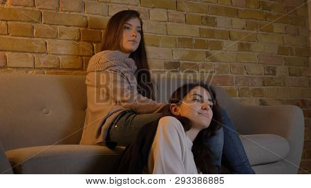 Closeup Portrait Of Two Young Pretty Women Watching A Movie Tv Sitting Laidback On The Floor In A Co