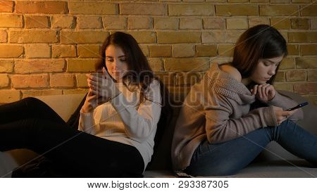 Closeup Portrait Of Two Young Pretty Caucasian Girls Browsing On The Phones While Resting On The Cou
