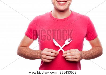 Smiling Handsome Guy Holding Plastic Fork And Knife Near His Stomach Over White Background. Studio S