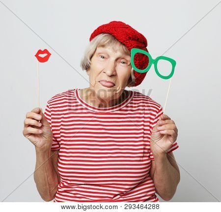 lifestyle, people and party concept: funny grandmother wearing red clothes holding falce glasses and  ready for party