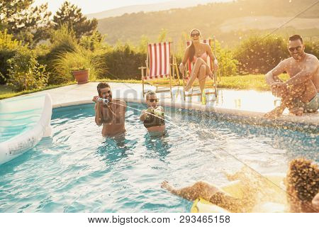Group Of Friends At A Poolside Summer Party, Having Fun In The Swimming Pool, Drinking Beer And Spla