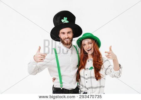 Happy young couple wearing costumes, celebrating St.Patrick 's Day isolated over white background, pointing fingers