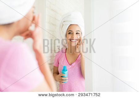 Woman Looking At Her Reflection And Applying Cream To Boost Hydration In Skin